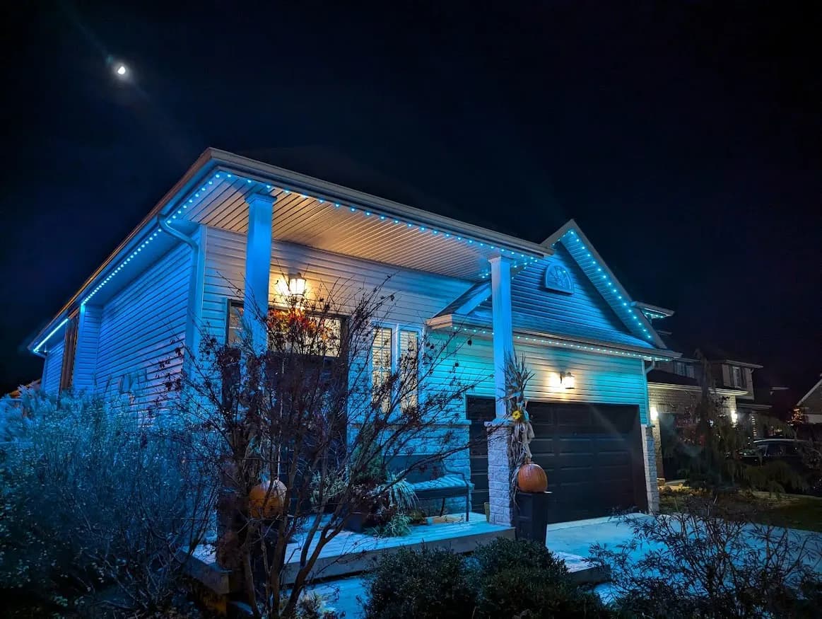 Two-storey brick home with permanent LED roofline lights glowing ice blue at dusk