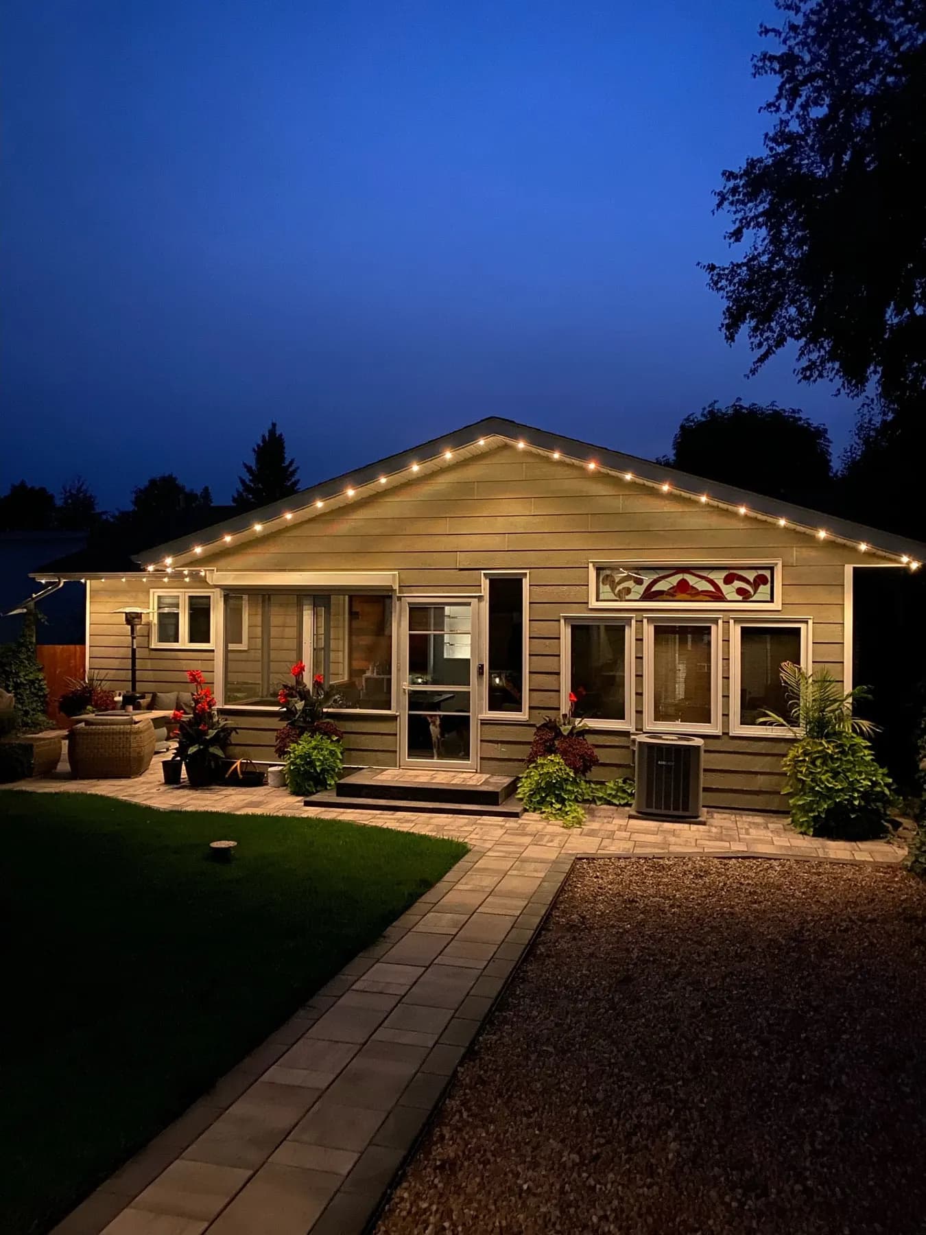 Snow-covered roofline of a Canadian home with black aluminum permanent LED track and warm white puck lights glowing along the eaves